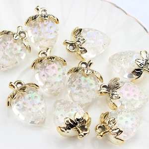 Translucent iridescent strawberry charms with gold leaves on a white textured plate