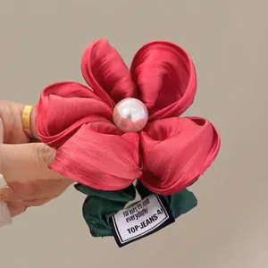 Close-up of red floral hair scrunchie with satin petals, pearl center and green leaf detail