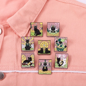 Detailed enamel pins featuring black cat tarot cards on pink denim fabric background
