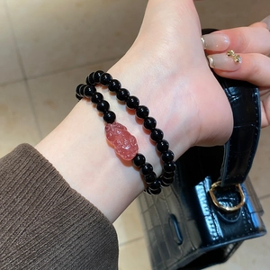 Detail of beaded bracelet set with pink PiXiu charm on a hand holding a black purse