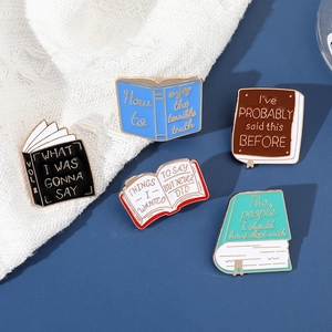 Detailed view of five colorful metal book pins with creative English quotes on fabric