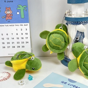 Close-up of green plush turtle keychain with metal bead chain on a decorative desk