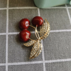 Macro de la broche cerise en émail rouge avec strass étincelants sur feuilles dorées