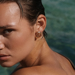 Eleganti orecchini a spirale dorati indossati da una modella su sfondo di acqua blu profonda