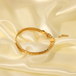 Détail d'un bracelet gourmette doré avec fermoir mousqueton sur un tissu en soie beige