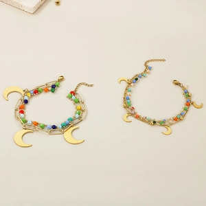 Detail of layered gold moon bracelets with colorful beads on minimalist stone background