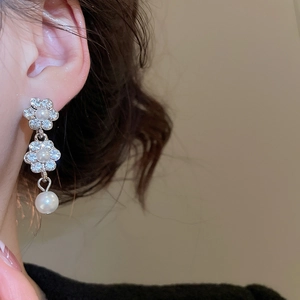 Detail of silver flower earrings with pearl drops worn by a model in natural light
