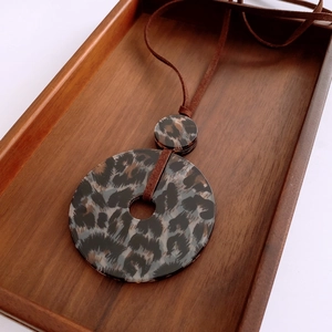 Detail of leopard print acrylic double ring pendant with a brown cord on wooden tray
