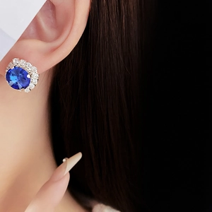 Close-up of blue gemstone stud earrings with crystal halo shown on model ear