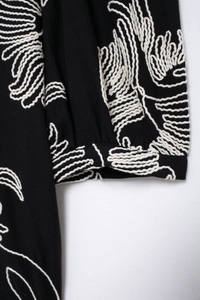 Close-up of white floral embroidery details on black short-sleeved cotton blouse
