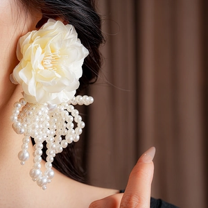 Detail of floral fabric earrings with white pearl tassels worn by a model