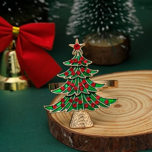 Close-up of a green enamel Christmas tree napkin ring with red rhinestones on a wood slice