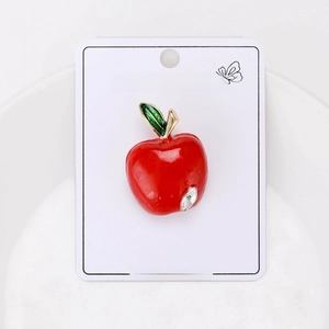 Detail shot of a red enamel apple brooch with a sparkling rhinestone on a display card