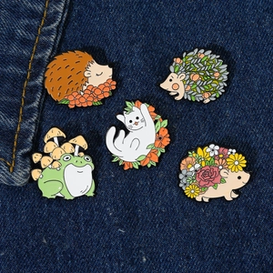 Five cute animal enamel pins including hedgehog and cat on blue denim fabric background