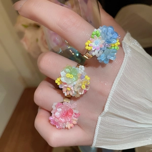 Dettaglio di anelli floreali in resina e perline blu rosa e gialli sulla mano della modella