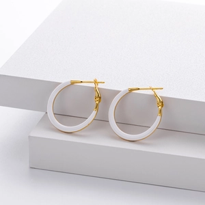 Detail of gold and white enamel hoop earrings on minimalist white textured cubes