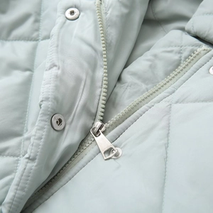 Detailed macro view of high-quality zipper and quilted fabric on light blue coat