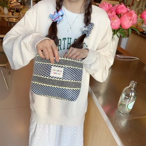 Detail of colorful striped woven makeup bag being used by model in a bright room