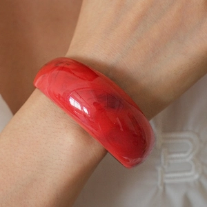 Close-up of a wide red resin bangle with marble texture worn on a wrist