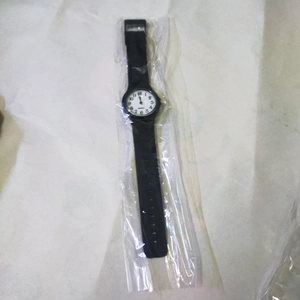 Detail view of a black quartz watch with silicone strap in protective plastic packaging