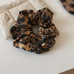 Détail d'un chouchou léopard avec un nœud en cuir noir et un ornement métallique