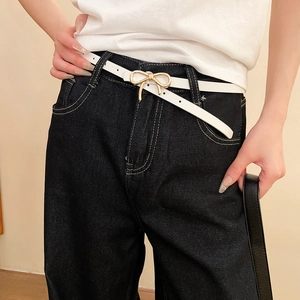 Detail of white leather skinny belt featuring a golden bow-shaped metal buckle on denim