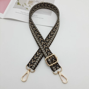 Detail of adjustable woven bag strap featuring a black and brown arrow pattern with gold clips