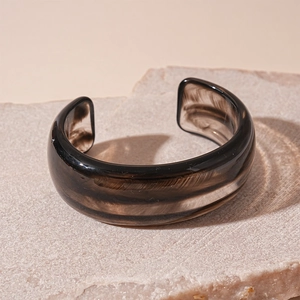 Detail eines lichtdurchlässigen rauchbraunen Acryl-Armreifs mit Naturtextur auf Stein
