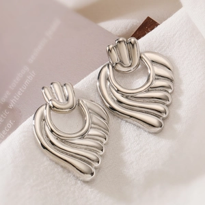 Minimalist silver wavy shell-shaped metal earrings on a soft white fabric background