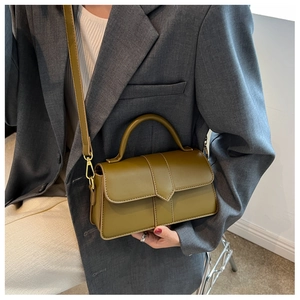 Detail of green leather handbag with gold hardware and detachable shoulder strap on grey blazer