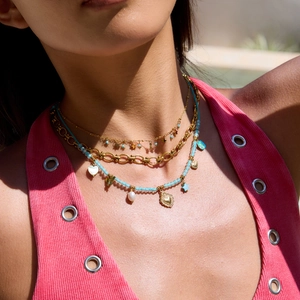 Layered gold necklaces with turquoise beads, heart and star charms worn by a model