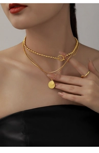 Close-up of three-layer gold necklace with coin pendant and matching ring on model