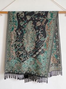 Detailed view of dark cashmere scarf featuring green paisley patterns and fringe edges