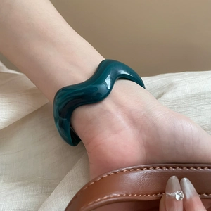Close-up of a dark green wavy acrylic cuff bracelet featuring a high-gloss glazed finish