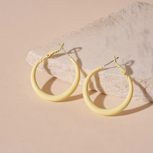 Detailed close-up of cream yellow geometric hoop earrings on a beige textured stone base