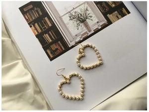 Detail shot of heart-shaped pearl drop earrings on white silk fabric background