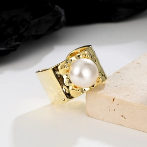 Detail of wide gold ring with large round pearl and hammered texture on beige stone
