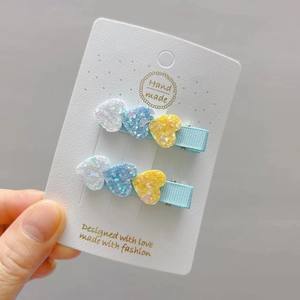 Close-up of glitter heart hair clips in white, blue and orange on handmade card