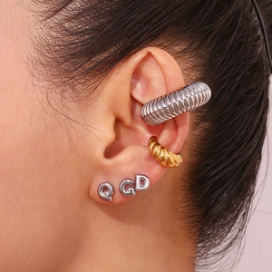Close-up of golden textured ear cuffs and silver initial studs on a woman's ear