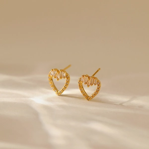 Macro shot of gold heart earrings with white zircons on beige silk background