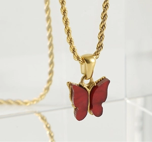 Macro view of gold rope chain and vibrant red butterfly pendant on clear display