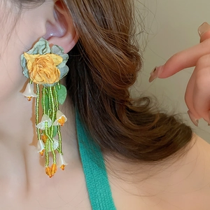 Détail de boucles d'oreilles muguet avec fleur en tissu jaune et glands en perles