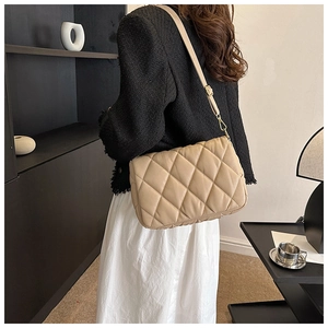 Detail of khaki quilted shoulder bag with adjustable strap worn by a model in modern interior