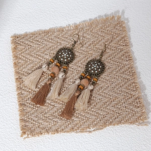 Detailed view of bohemian feather fringe earrings on natural linen background