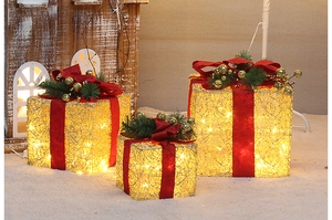 Close-up of golden LED Christmas gift boxes with red bows and pine needles on snow