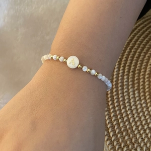 Close-up of beaded bracelet featuring white beads and a golden letter A charm on a wrist