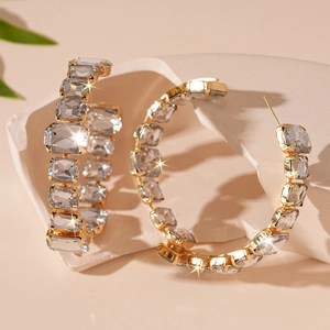 Close-up of golden C-shaped hoop earrings with emerald-cut crystals on stone background