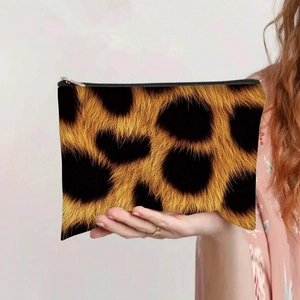Leopard print canvas makeup bag with zipper closure held by hand against solid wall