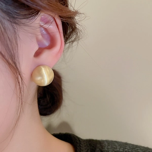 Close-up of a minimalist round gold bead stud earring worn by a model in a side view