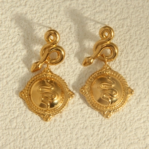 Vintage gold snake earrings with embossed serpent pendant on textured wall background
